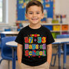A young boy smiling in a brightly lit classroom, wearing a black t-shirt with a colorful '67 + 33 Days of School' graphic print.