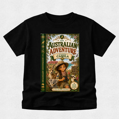 A black short-sleeve t-shirt with a large graphic print on the front depicting a book cover titled 'The Australian Adventure: Starring Camila'. The graphic features an illustration of a young girl in a safari outfit with a koala and a kangaroo, set against a light gray textured background.