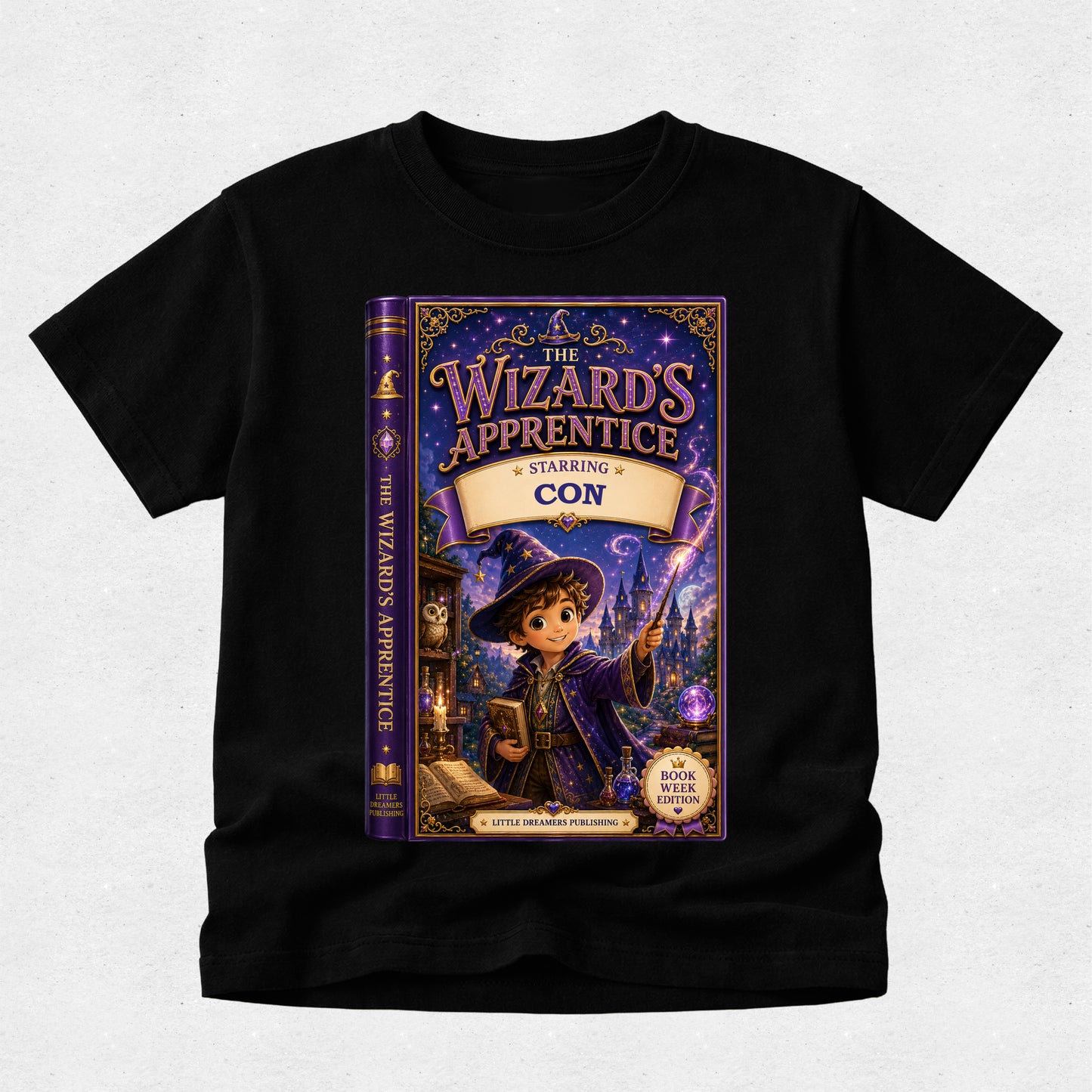 A black short-sleeve t-shirt with a large graphic print of the book cover for 'The Wizard's Apprentice: Starling Con' on the front, displayed against a light gray textured background.