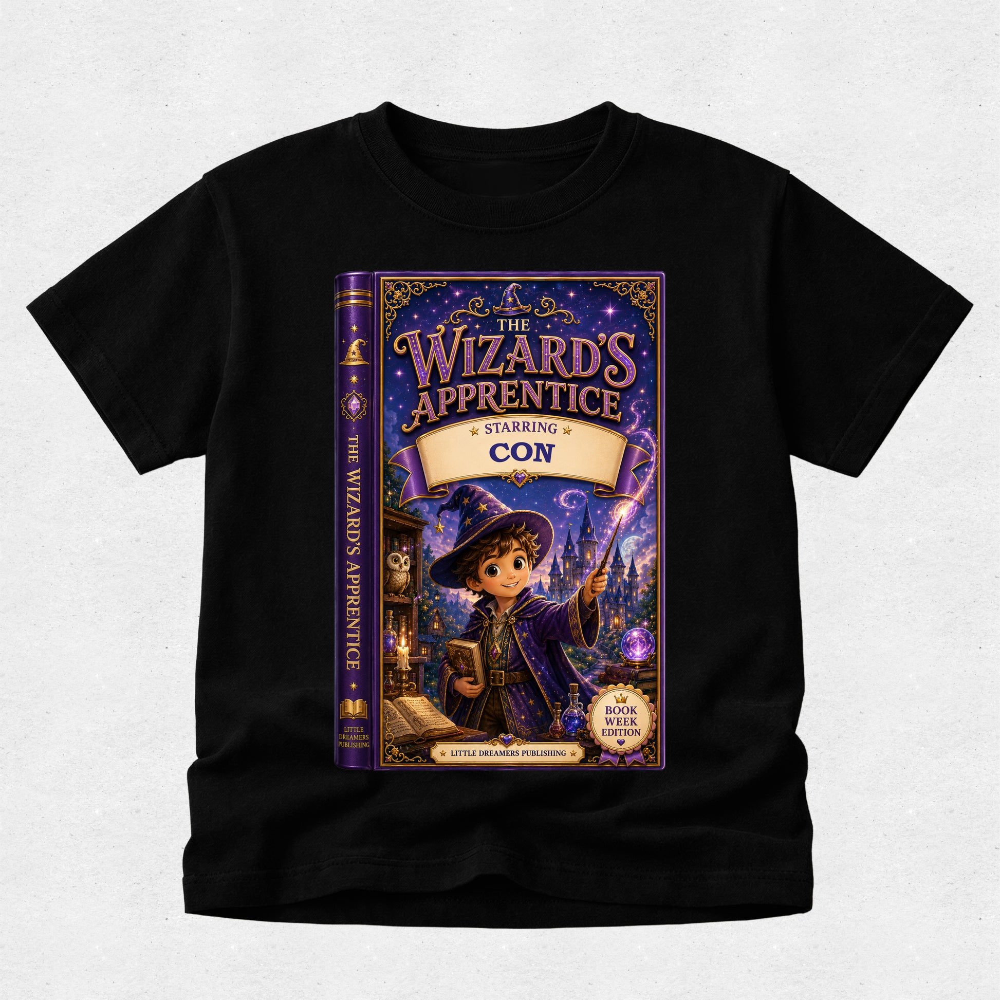 A black short-sleeve t-shirt with a large graphic print of the book cover for 'The Wizard's Apprentice: Starling Con' on the front, displayed against a light gray textured background.