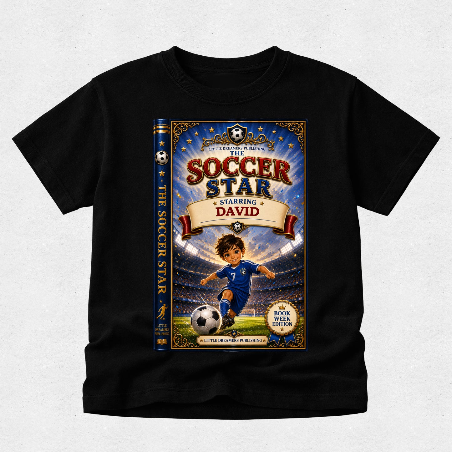 A black short-sleeve t-shirt with a large custom graphic print of a children's book cover titled 'The Soccer Star Starring David'. The graphic features an illustration of a boy in a blue soccer uniform on a field with a stadium background, and the book spine is shown on the left side of the cover.