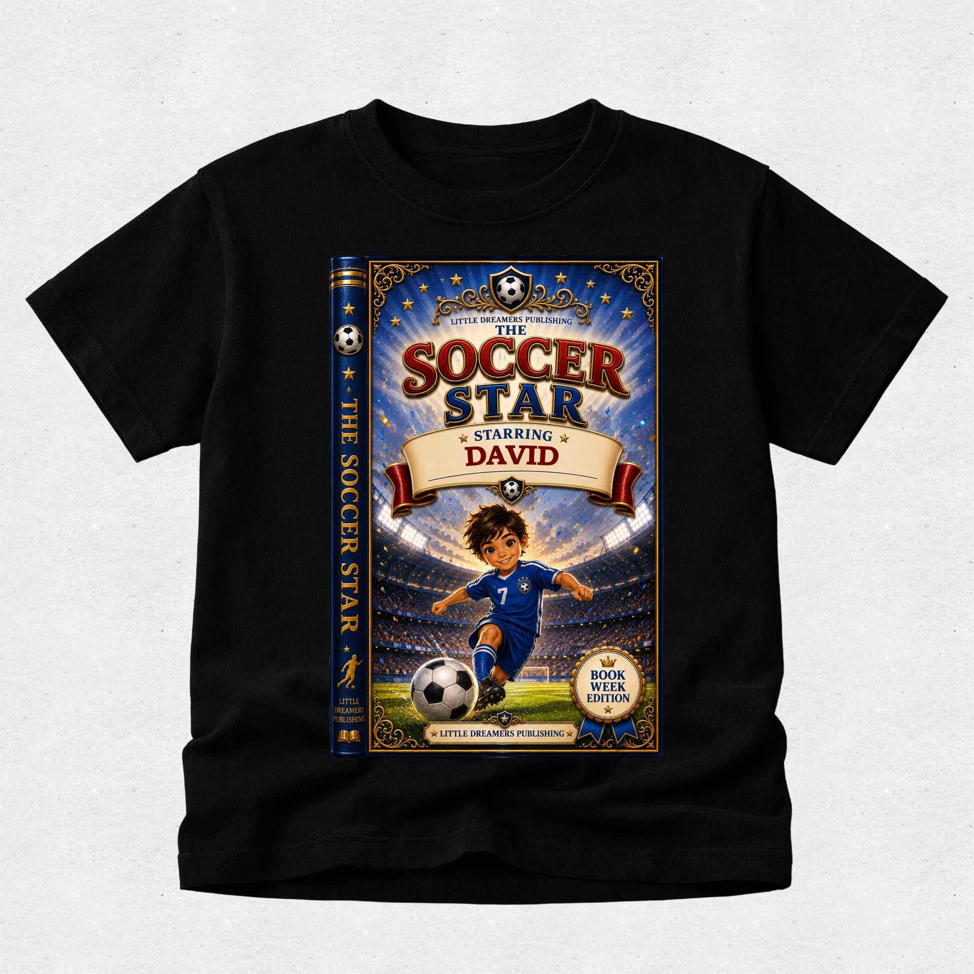 A black short-sleeve t-shirt with a large custom graphic print of a children's book cover titled 'The Soccer Star Starring David'. The graphic features an illustration of a boy in a blue soccer uniform on a field with a stadium background, and the book spine is shown on the left side of the cover.
