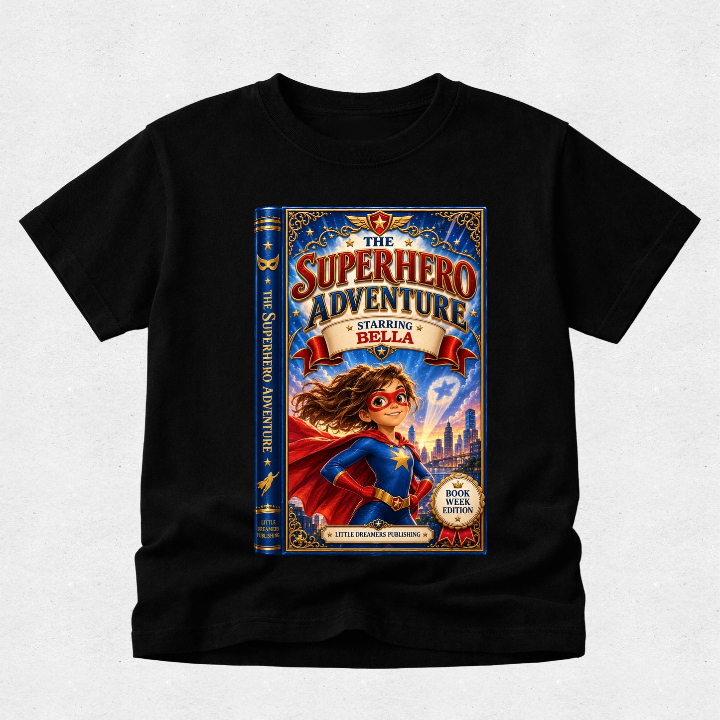 A black short-sleeve crewneck t-shirt featuring a large graphic print of a book cover titled 'The Superhero Adventure' with an illustration of a girl in a superhero costume, displayed on a light gray textured background.