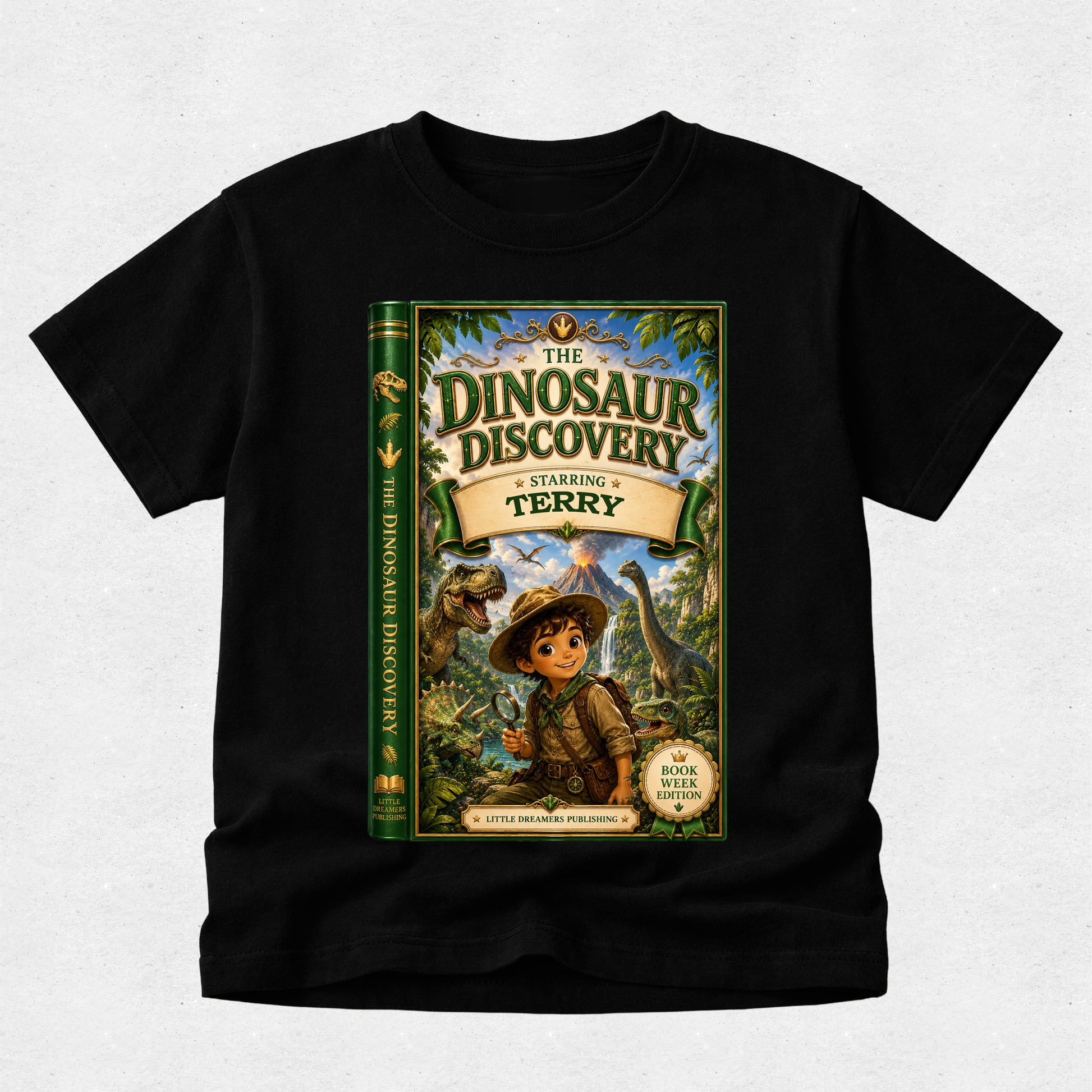 A black short-sleeve t-shirt with a large graphic print of a children's book titled 'The Dinosaur Discovery: Starring Terry' on the front, displayed against a light gray textured background.