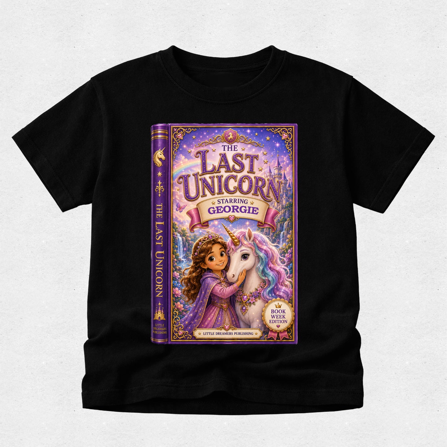 A black short-sleeve t-shirt with a large, colorful graphic print of the book cover for 'The Last Unicorn: Starring Georgie' on the front, displayed against a light gray textured background.