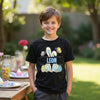 Child wearing a black t-shirt with colorful graphics and the name 'Leon' outdoors.