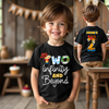 Child wearing a black t-shirt with colorful text and graphics, standing in a room with wooden furniture.