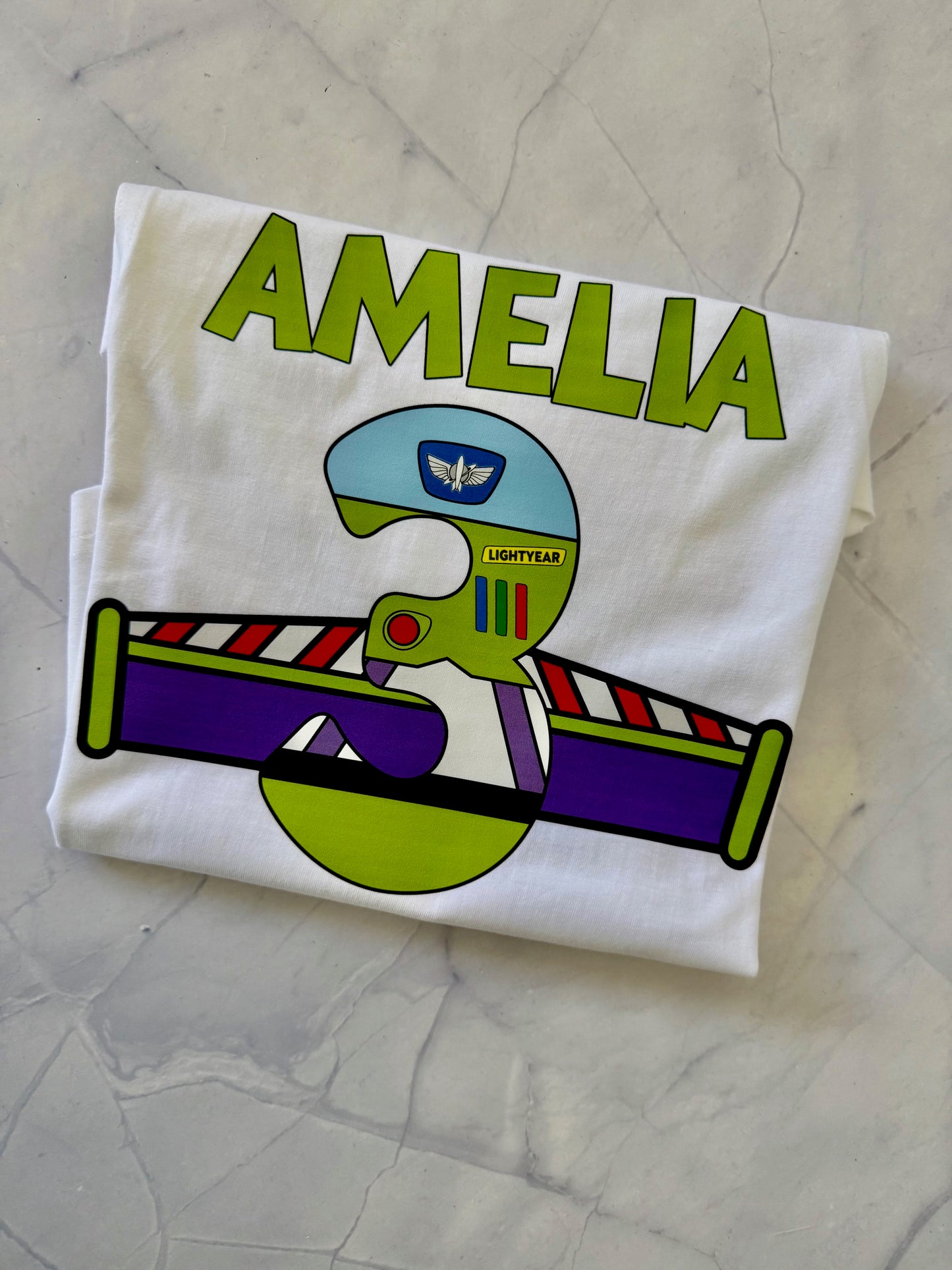 White t-shirt with a colorful design and 'Amelia' text on a textured surface