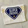 Folded white t-shirt with 'Super Freddie' design on a gray surface
