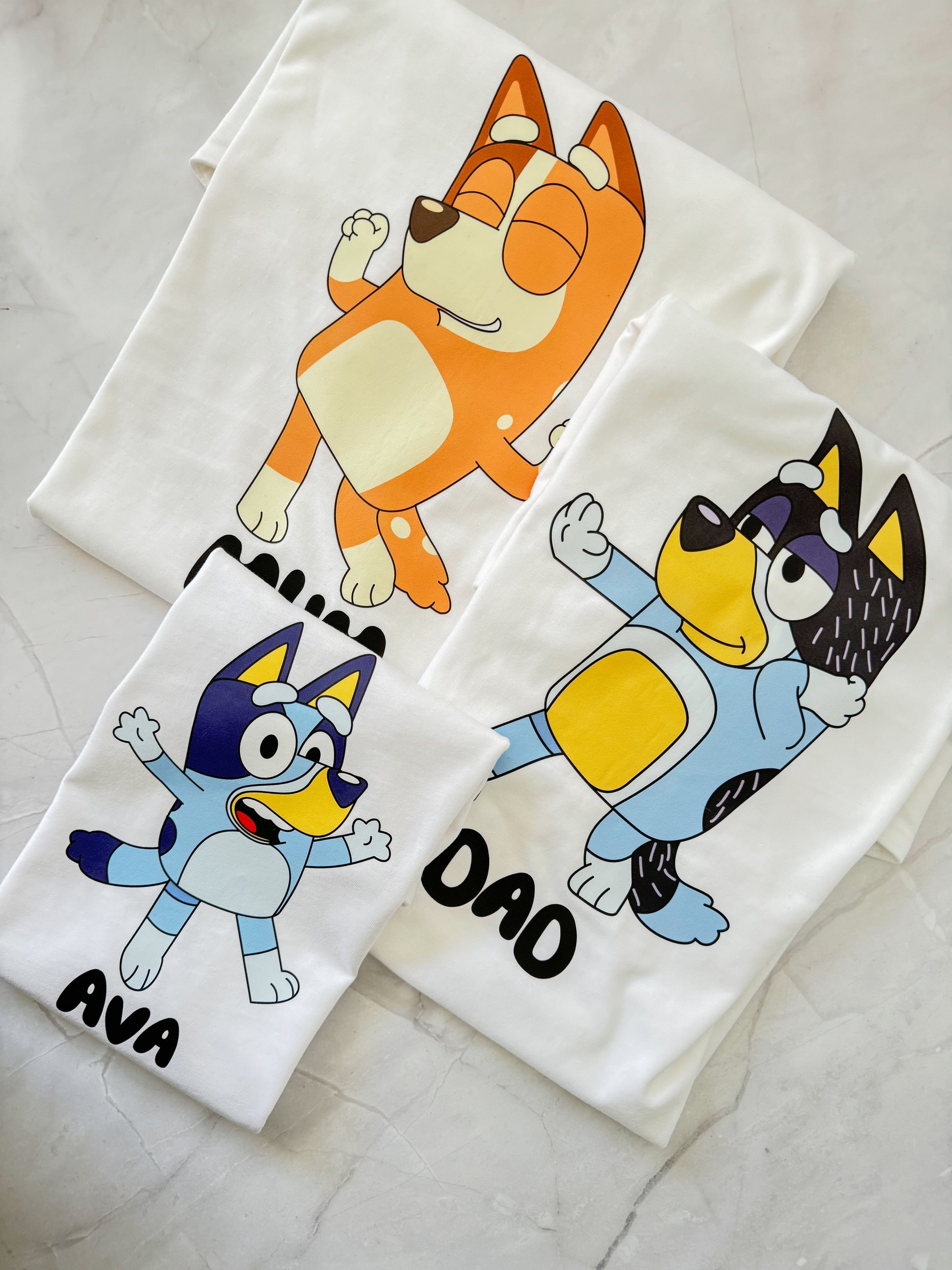 Flat lay showing different t-shirt color options with Bluey-inspired character graphics from Set 1.