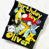 Black t-shirt with colorful cartoon characters and 'Birthday Boy Oliver' text on a white background