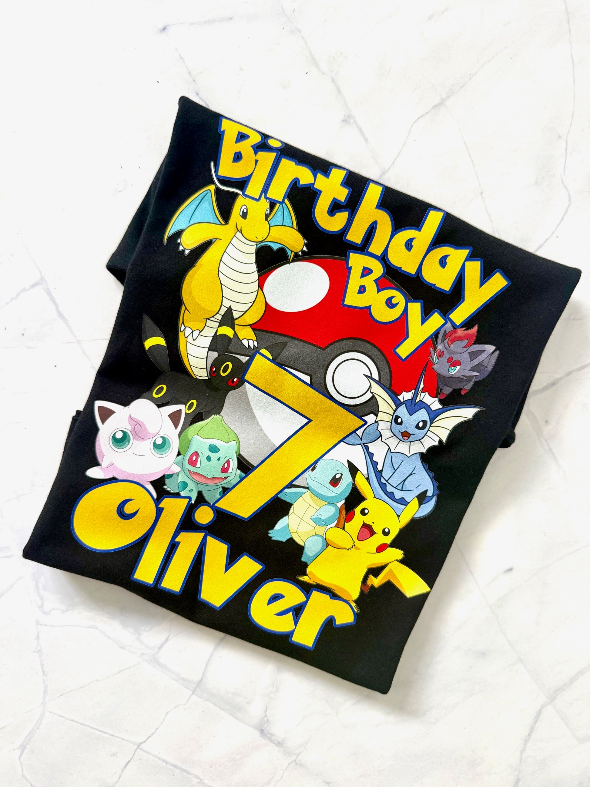 Black t-shirt with colorful cartoon characters and 'Birthday Boy Oliver' text on a white background