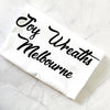 White shirt with 'Joy Wreaths Melbourne' text on a textured white surface