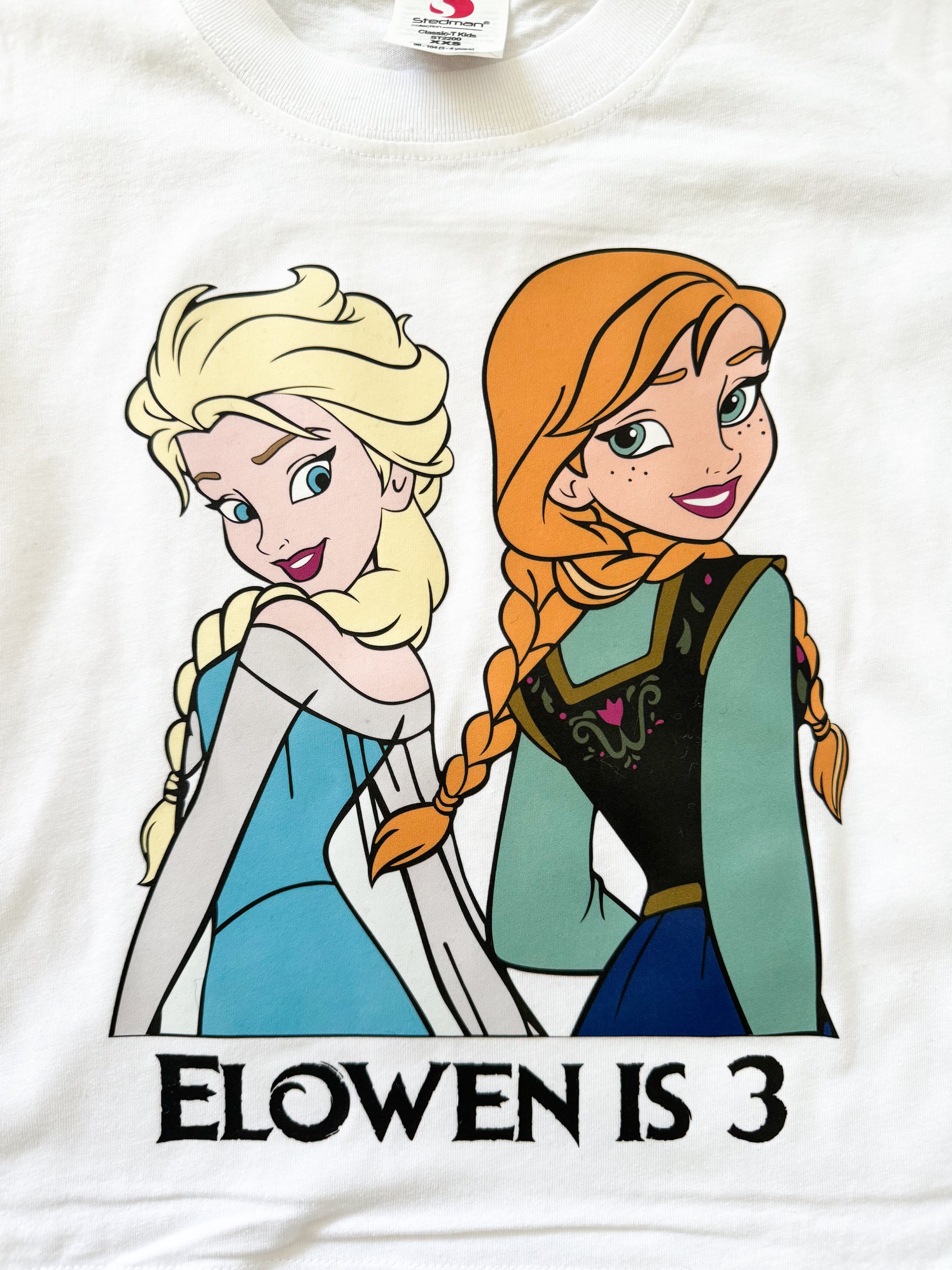 White t-shirt with cartoon characters and 'Elowen is 3' text on a white background