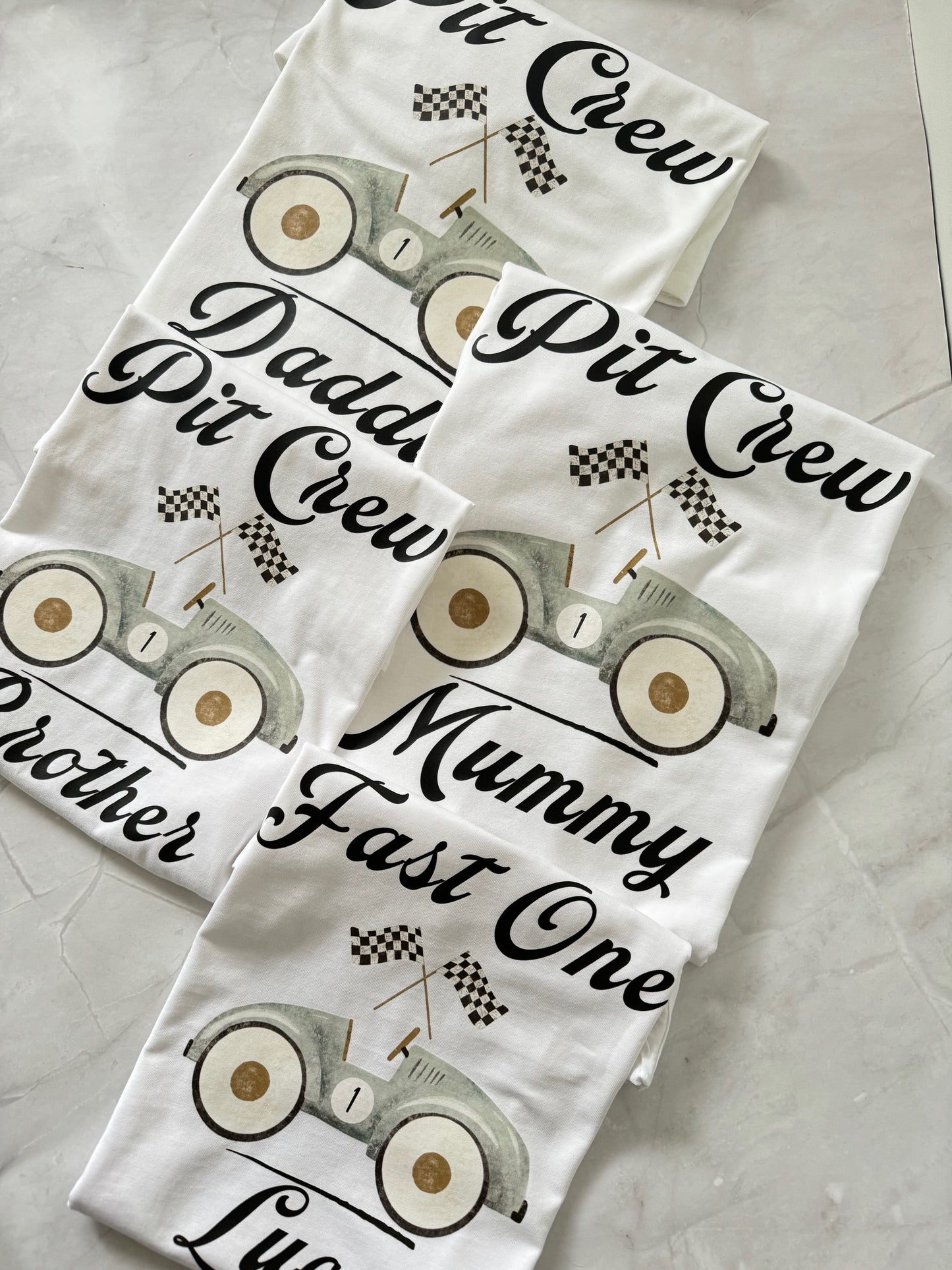 Stack of matching Race Day Pit Crew shirts labeled “Daddy Pit Crew,” “Brother Pit Crew,” and “Fast One.”