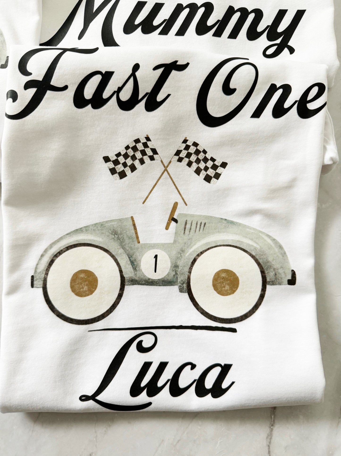 Close-up of “Mummy Fast One” t-shirt with vintage-style race car and checkered flags.
