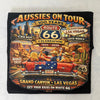 A black graphic t-shirt featuring a vintage-style 'Aussies on Tour 100 Years Route 66 Celebration' design with people in a red car on a desert road trip theme.