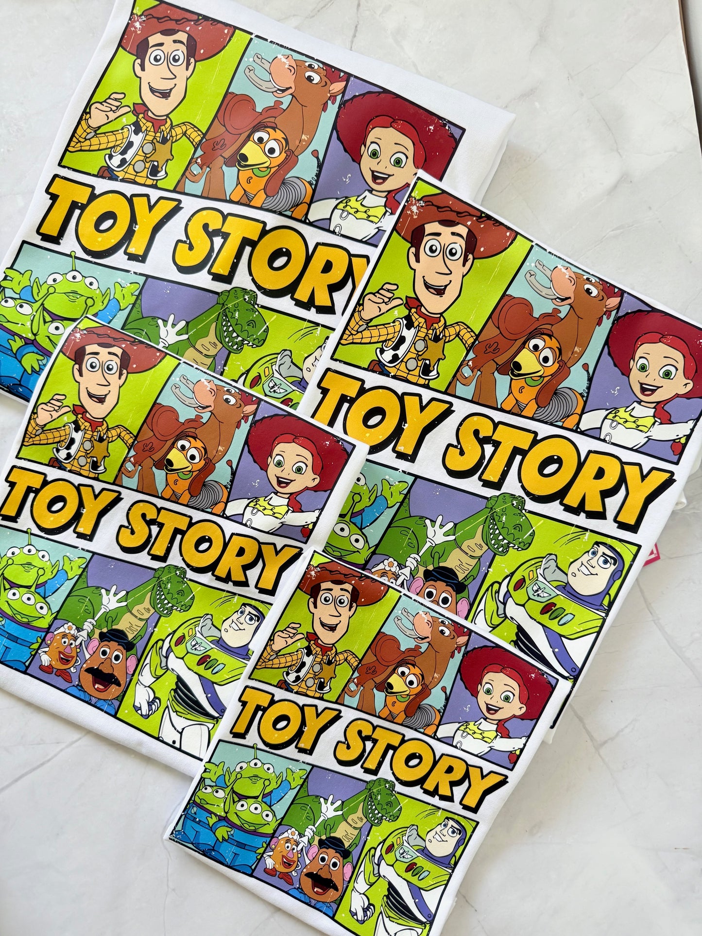  Flat lay of The Toy Box Crew family t-shirts featuring Toy Story-inspired design and playful colors.