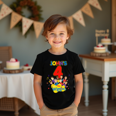 Child wearing a black t-shirt with colorful graphics and text, standing in a festive room with birthday cakes and decorations.