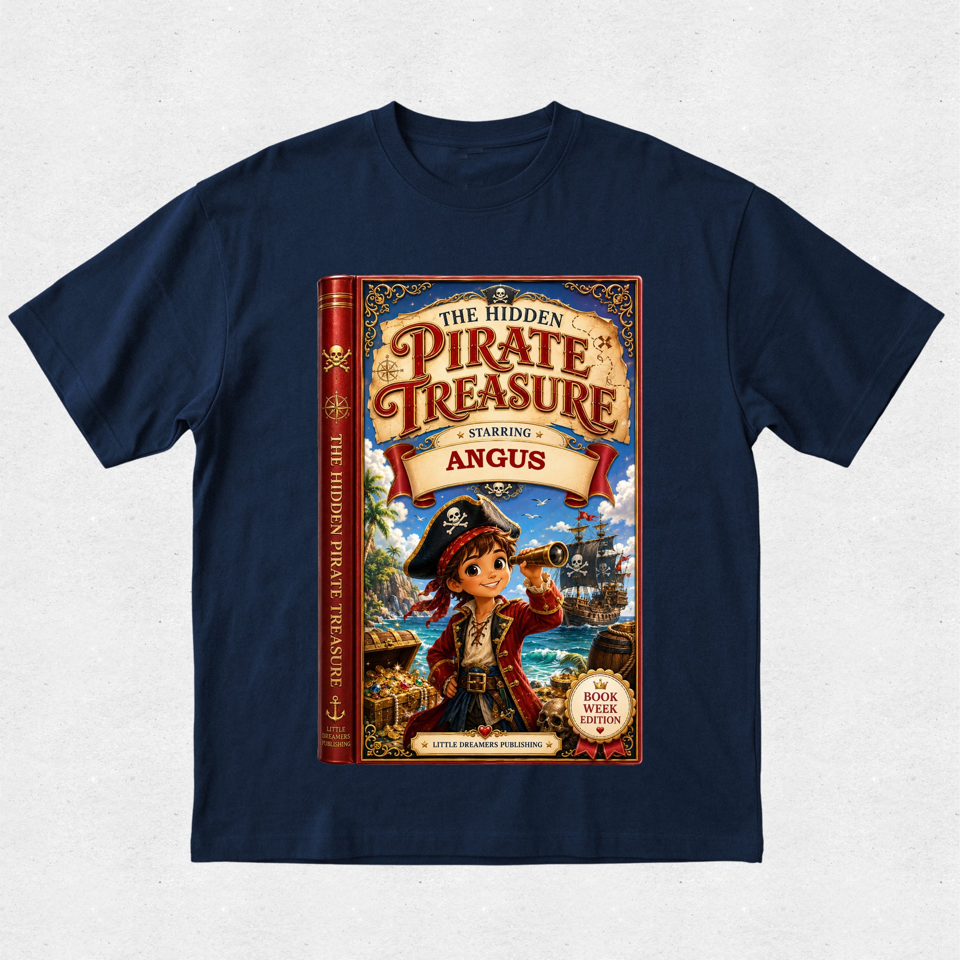 A navy blue short-sleeve t-shirt with a large graphic print of a children's book titled 'The Hidden Pirate Treasure Starring Angus'. The graphic shows a young boy in pirate clothing on the front cover, and the book spine is visible on the left side of the print.