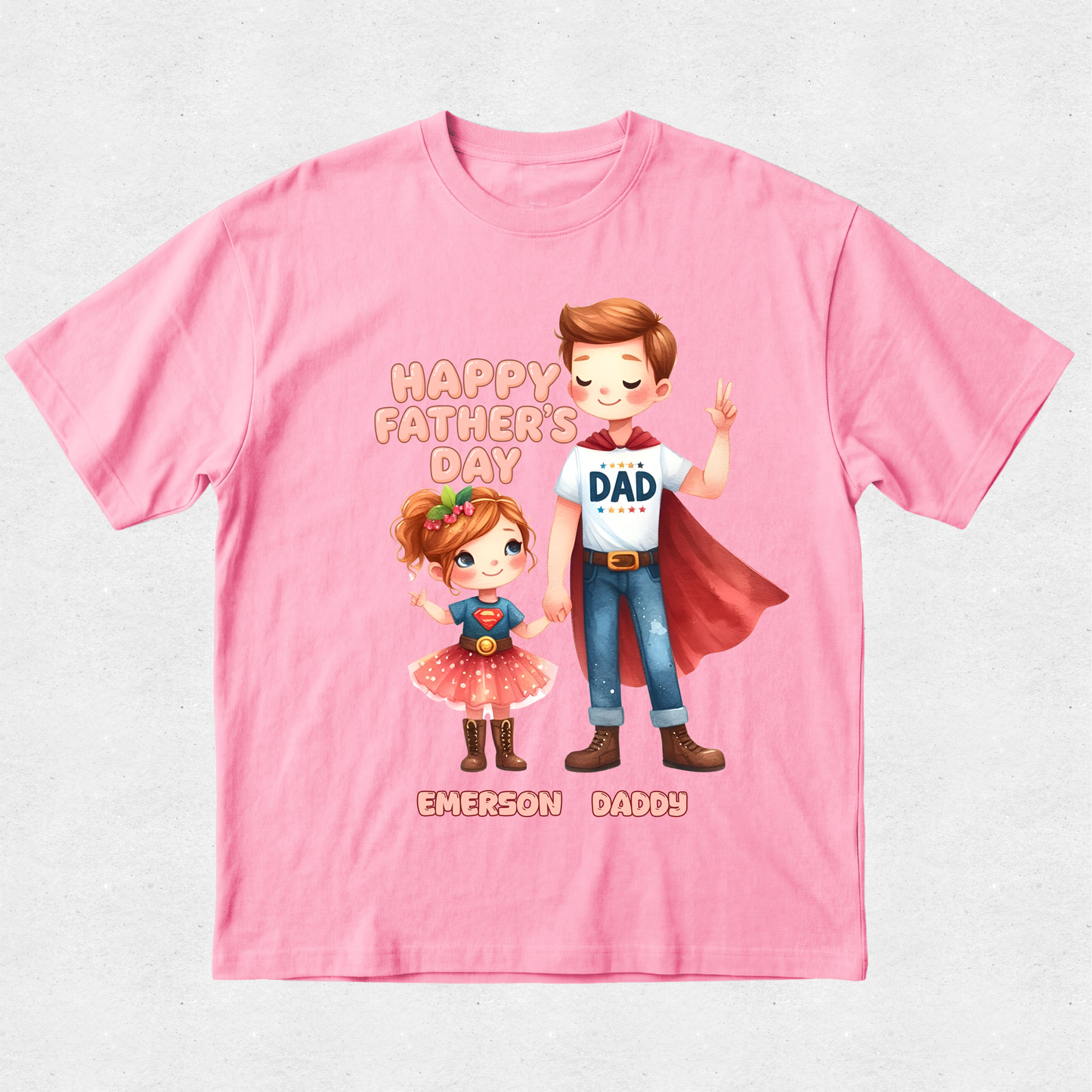 A pink short-sleeve crewneck t-shirt with a colorful graphic of a cartoon father and daughter in superhero costumes, with 'HAPPY FATHER'S DAY' and 'EMERSON DADDY' printed on the front.