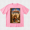 A pink short-sleeve crewneck t-shirt featuring a large graphic print of a book cover titled 'The Cowgirl Adventure: Fannie Figgle' on the front, displayed flat against a light gray textured background.