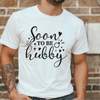 Person wearing a white t-shirt with 'Soon to be hubby' text against a brick wall.
