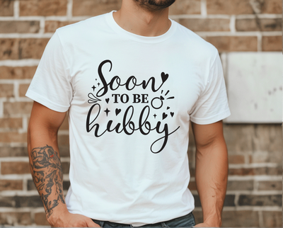 Person wearing a white t-shirt with 'Soon to be hubby' text against a brick wall.