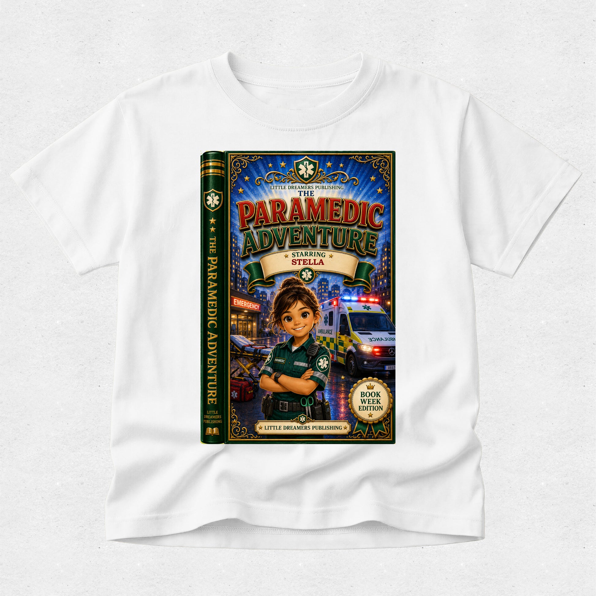 A white kids' t-shirt with a large graphic print of a book cover titled 'The Paramedic Adventure: Saving Stella' on the front, displayed on a light gray textured background.