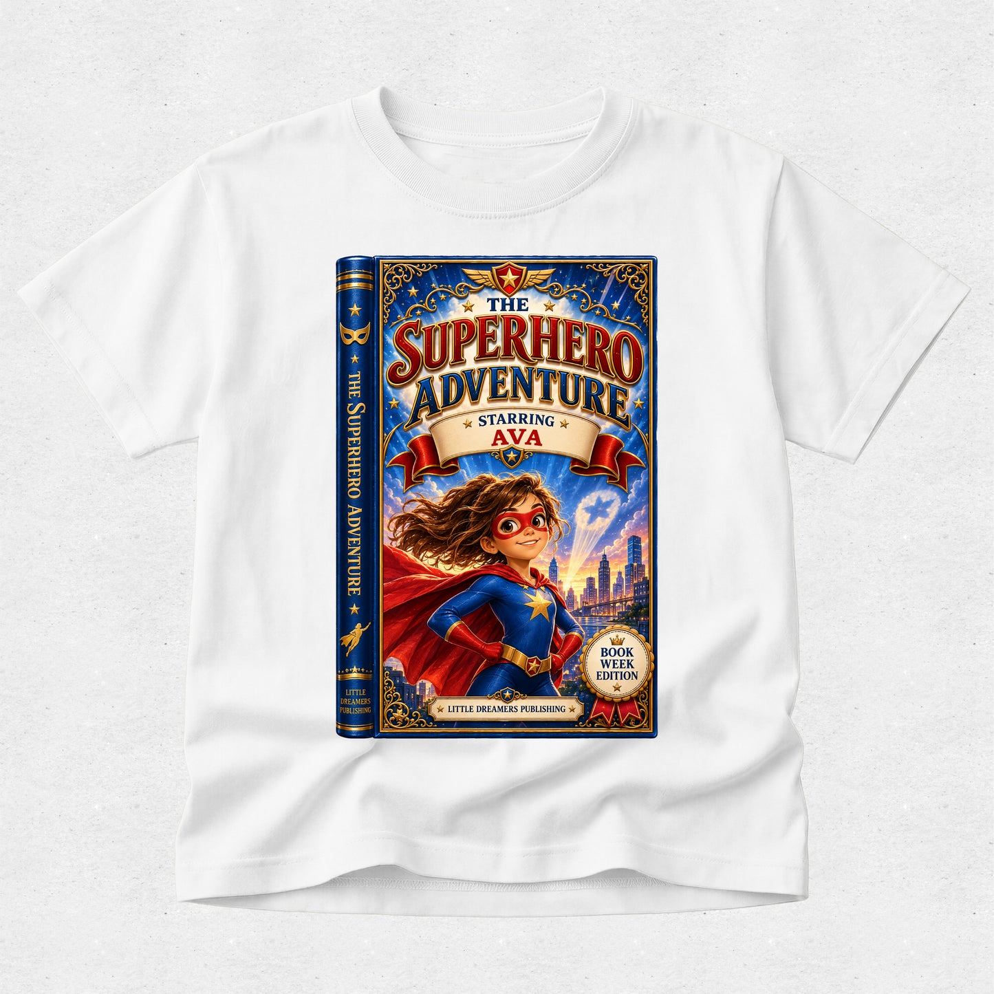 A white kids' t-shirt featuring a large graphic print of a book cover titled 'The Superhero Adventure' with a superhero character in a blue and red costume, displayed on a light gray textured background.