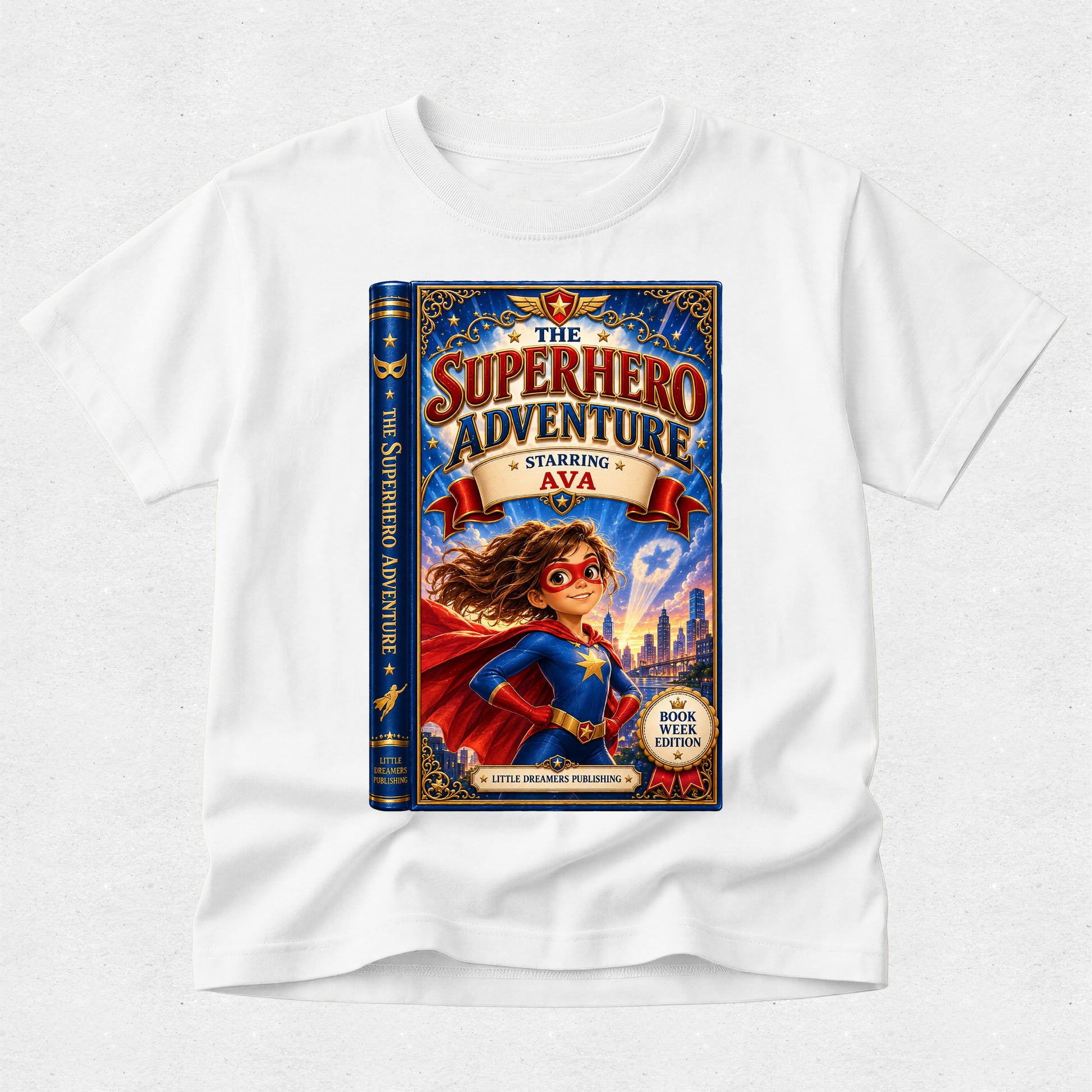 A white kids' t-shirt featuring a large graphic print of a book cover titled 'The Superhero Adventure' with a superhero character in a blue and red costume, displayed on a light gray textured background.