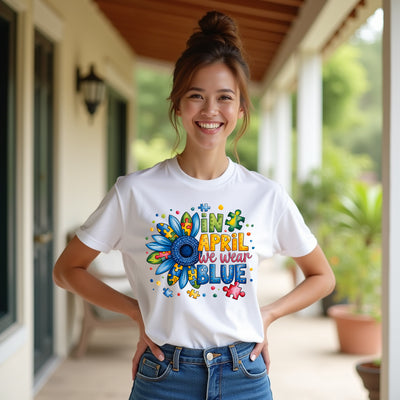 Woman wearing a white t-shirt with a colorful autism awareness design and text, standing on a porch.