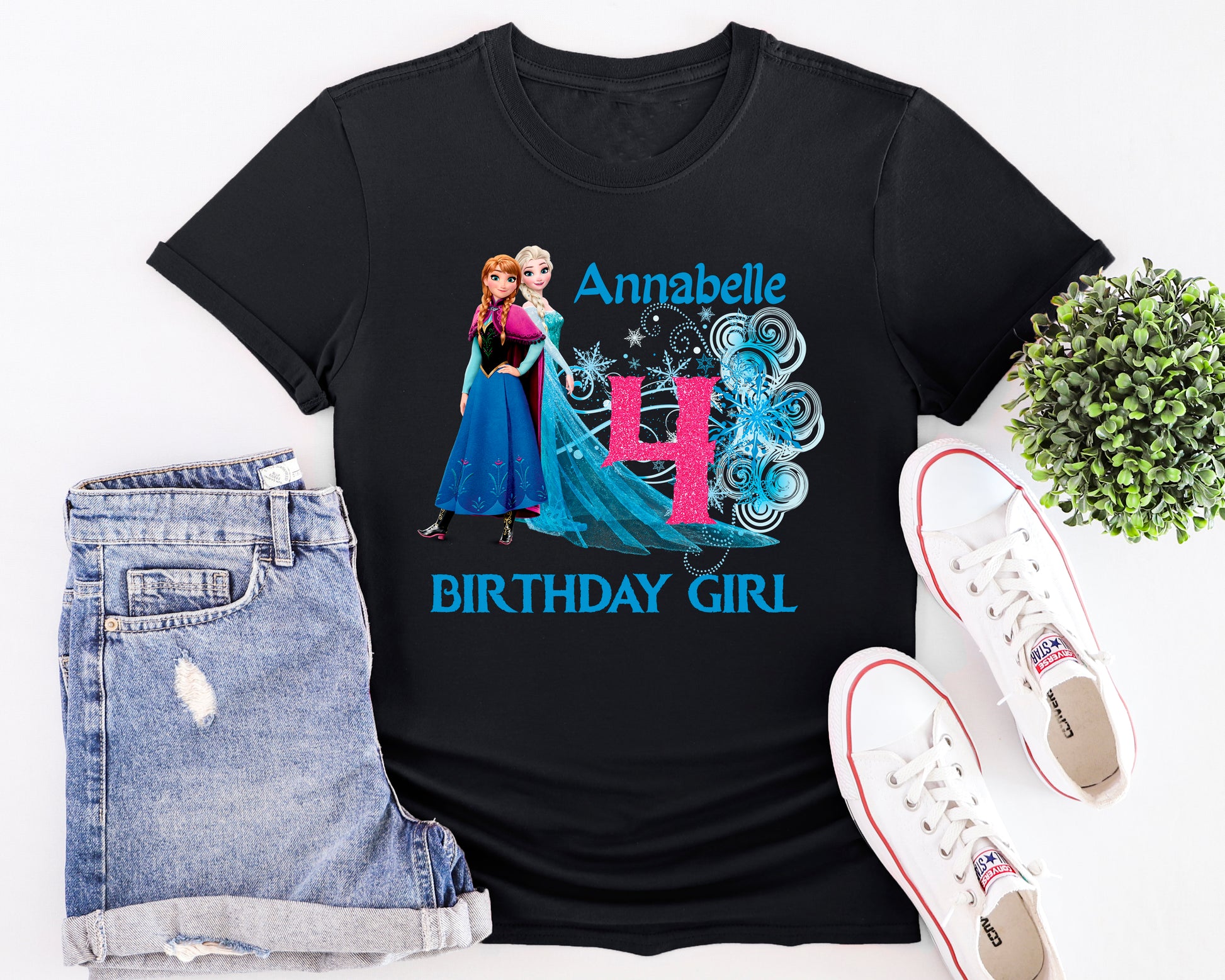 Black t-shirt with Frozen-themed design, denim shorts, and white sneakers on a white background