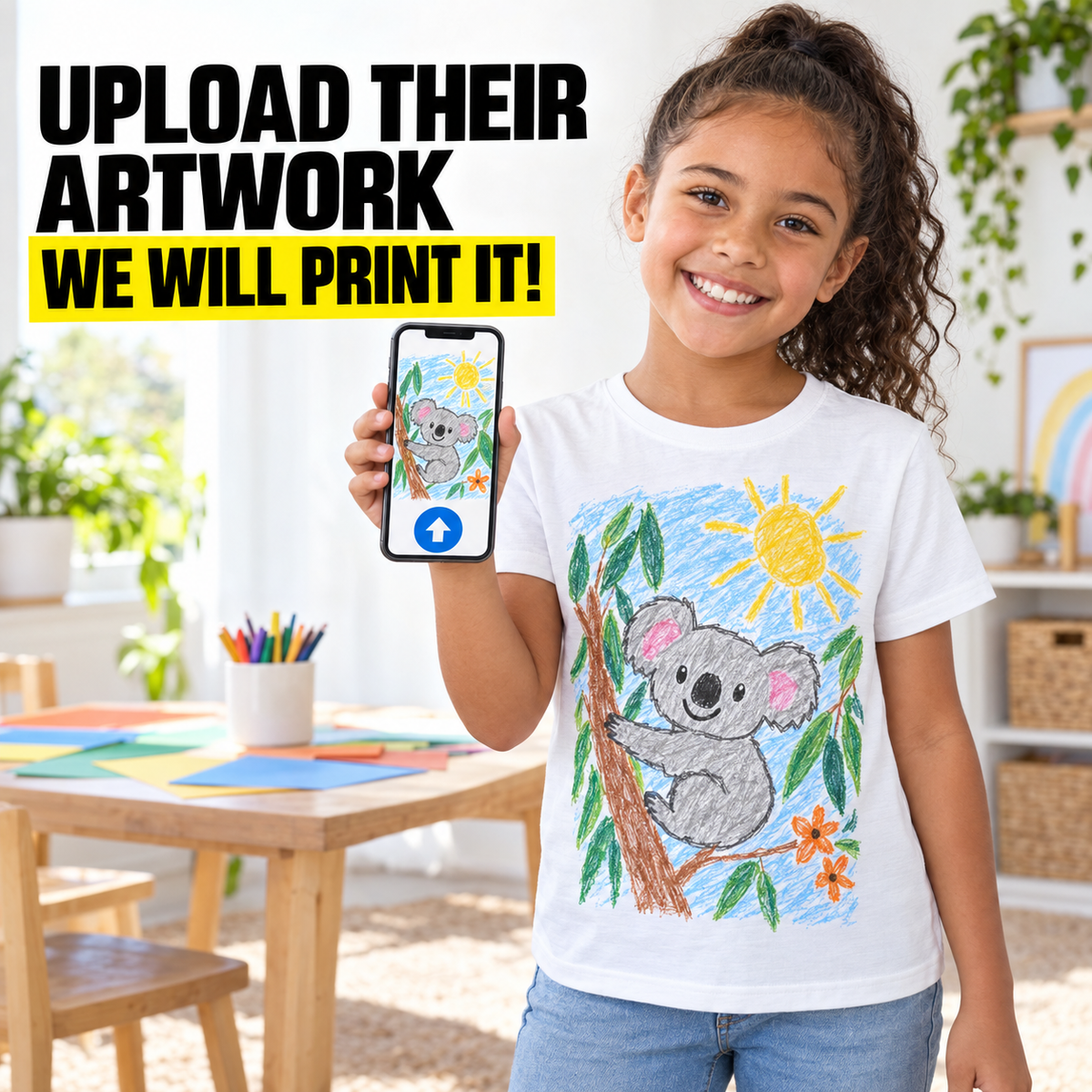 A smiling young girl stands in a bright room holding up a smartphone that displays a koala drawing, with large promotional text reading 'UPLOAD THEIR ARTWORK WE WILL PRINT IT!' at the top. She is wearing a white T-shirt with a colorful koala artwork printed on the front and blue jeans.