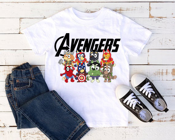 White t-shirt with Avengers cartoon characters, blue jeans, and black sneakers on a wooden surface