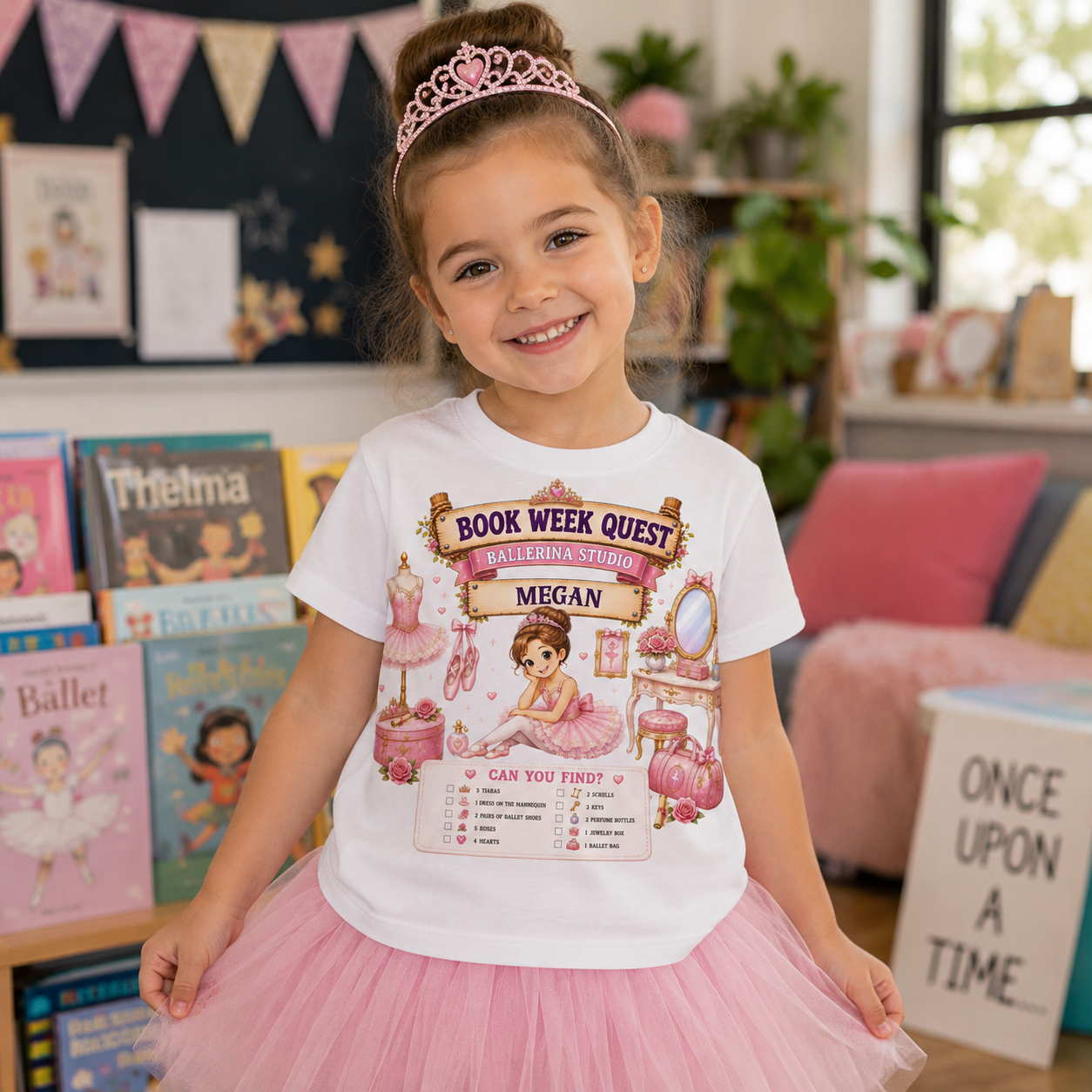 A young girl with a tiara and pink tutu stands in a decorated room wearing a white graphic T-shirt that says 'Book Week Quest' with a pink fairy illustration and checklist. The background shows books, bunting, plants, and a cozy interior.