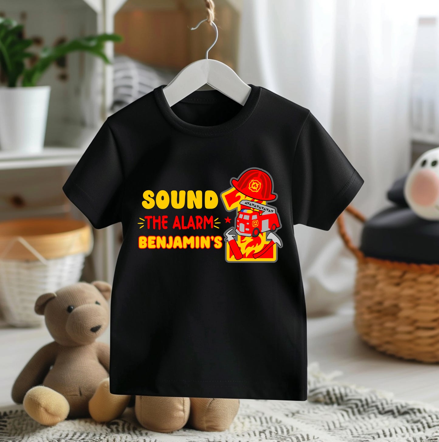 Black t-shirt with a fire truck graphic and text on a hanger in a room setting.
