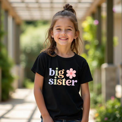Young girl wearing a black 'big sister' t-shirt with a flower graphic, standing outdoors.