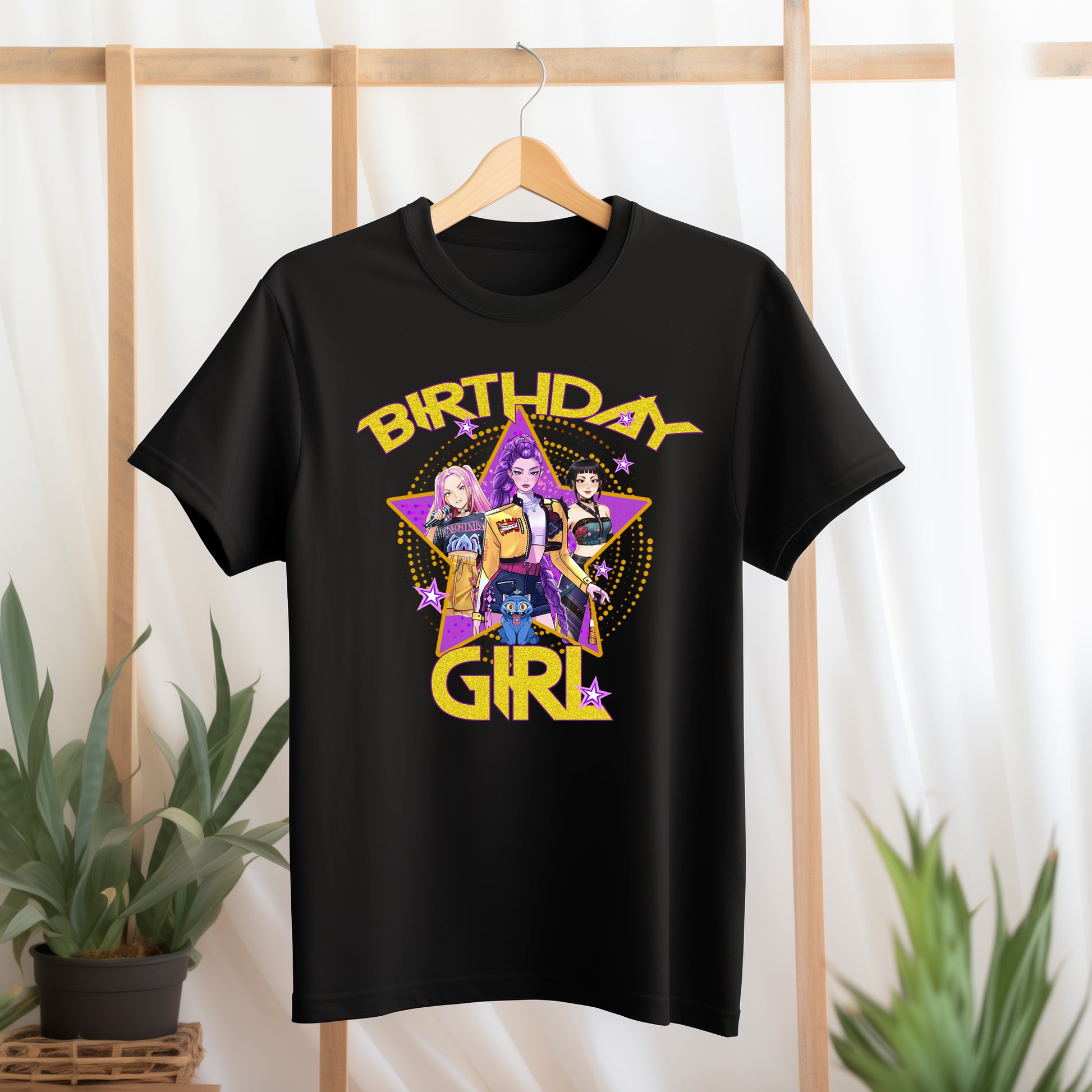 Black t-shirt with 'Birthday Girl' design featuring three girls and a purple triangle on a wooden rack.