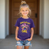 Young girl wearing a purple 'Birthday Girl' t-shirt with a star design, standing in front of a wooden door. kpop demon hunters