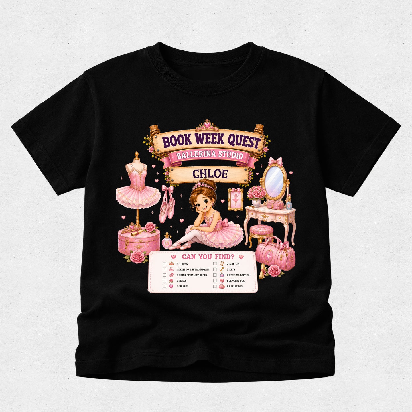 A black short-sleeve t-shirt with a detailed graphic print on the front. The graphic features a pink and gold 'Book Week Quest' banner with 'Ballerina Studio' and 'Chloe' written on it, surrounded by illustrations of a ballerina, a pink tutu, a vanity table, and a pink handbag, with a checklist below reading 'Can You Find?'.