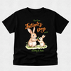 A black short-sleeve t-shirt with a custom Father's Day graphic featuring two rabbits eating carrots, with the text 'Our First Father's Day 2026' and 'Daddy & Nate' in green and orange lettering.