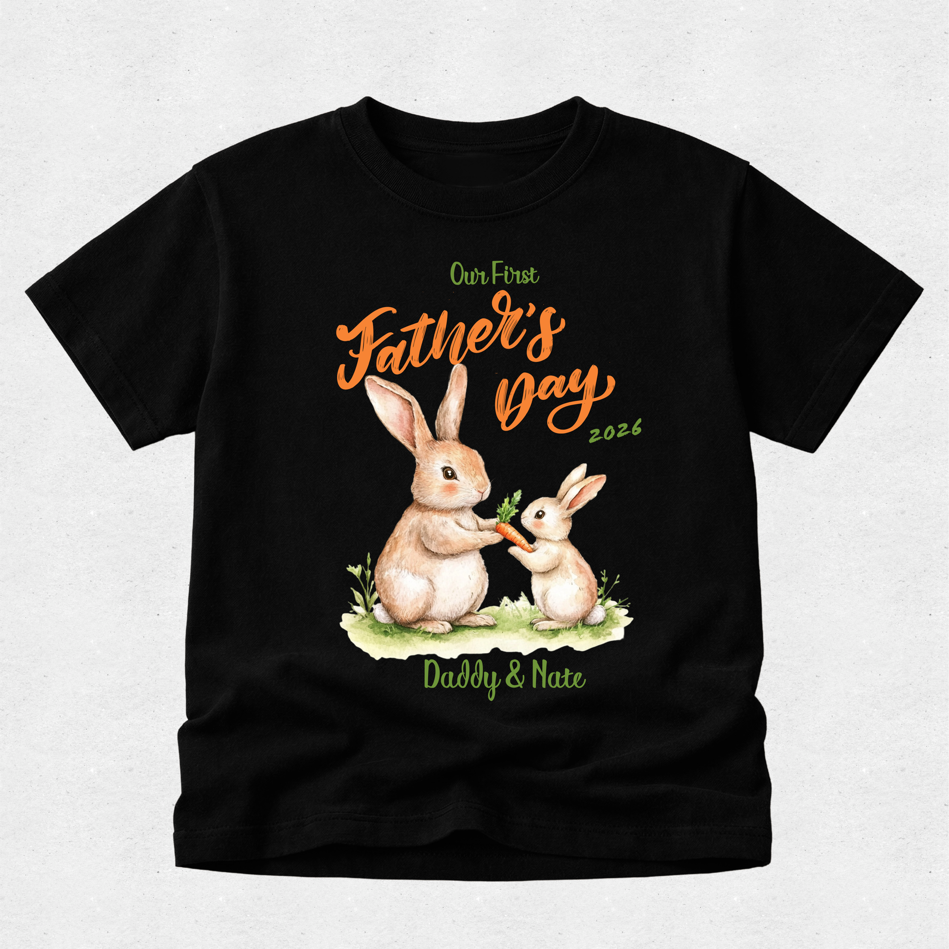 A black short-sleeve t-shirt with a custom Father's Day graphic featuring two rabbits eating carrots, with the text 'Our First Father's Day 2026' and 'Daddy & Nate' in green and orange lettering.