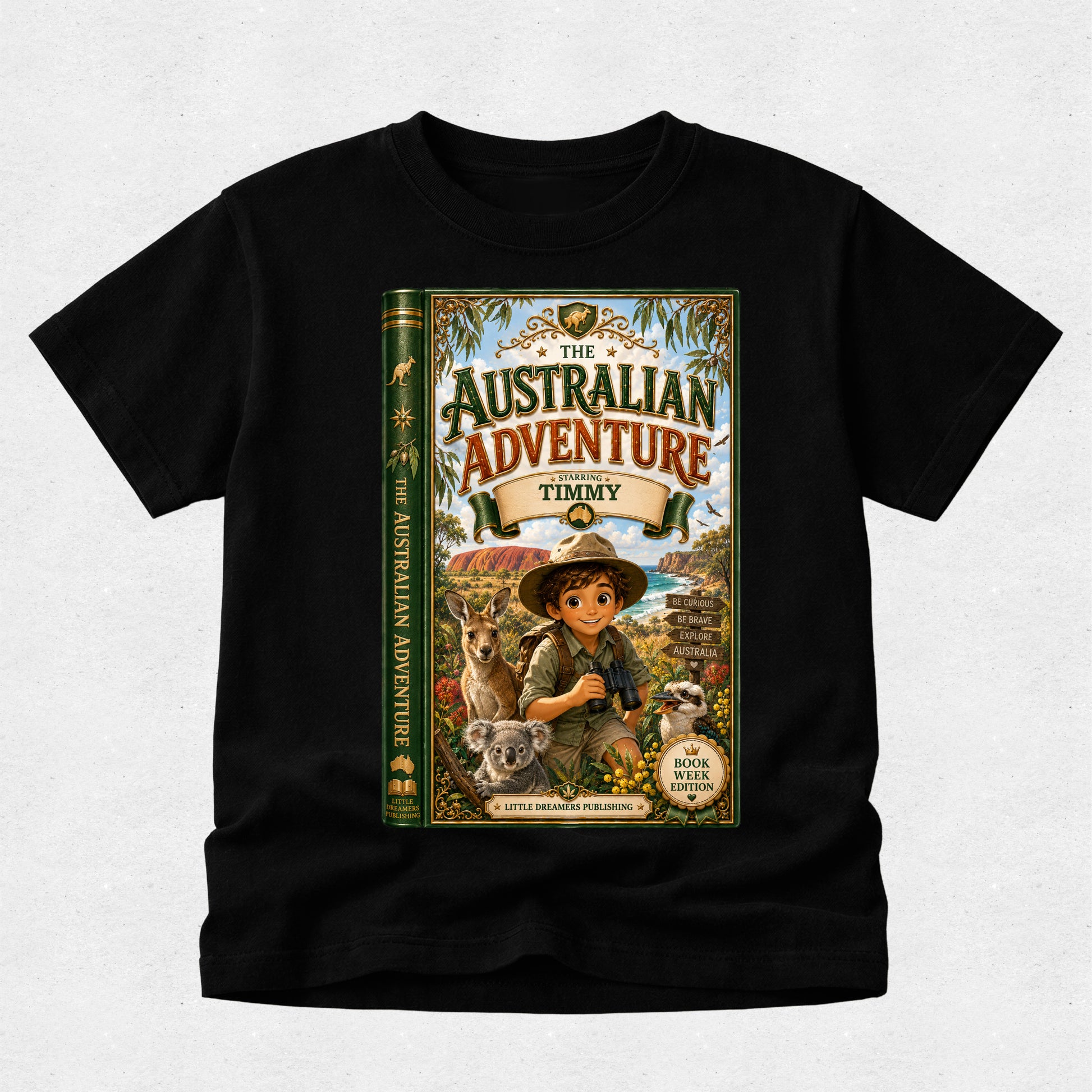 A black short-sleeve crewneck t-shirt featuring a large graphic print of a children's book titled 'The Australian Adventure' by Timmy, displayed on a light gray textured background.