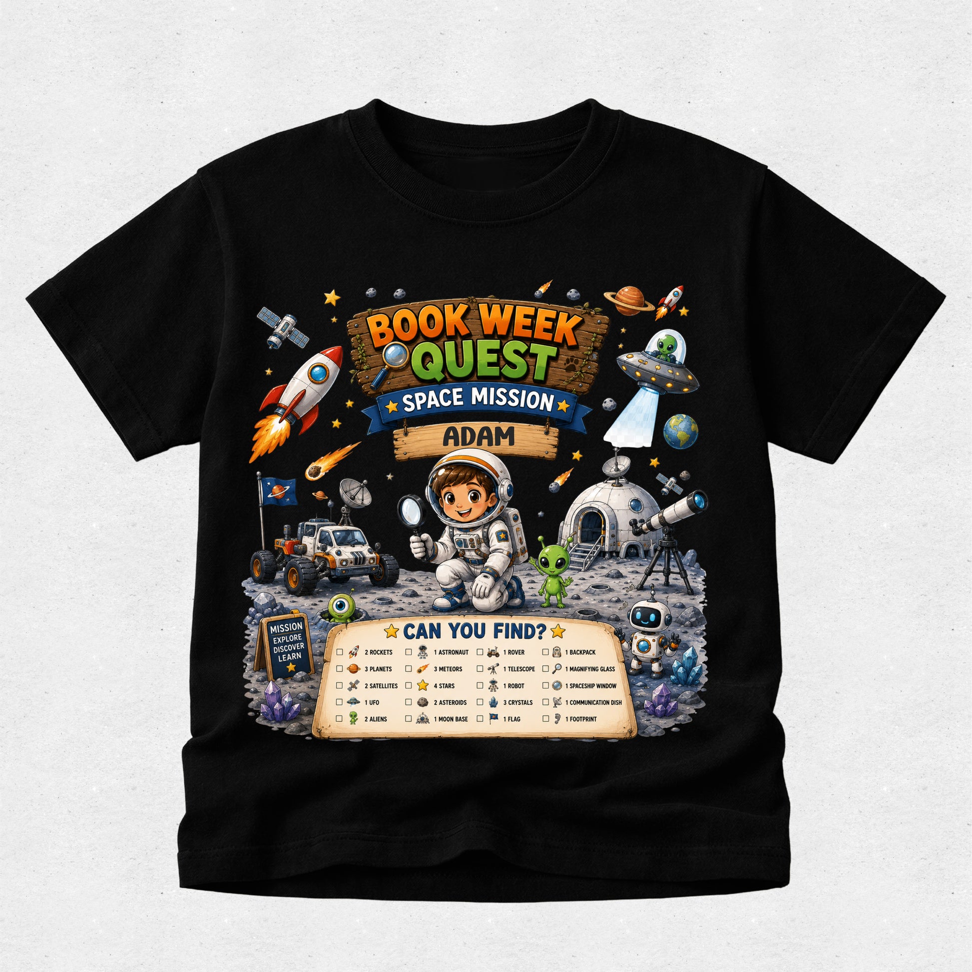 A black short-sleeve t-shirt with a colorful graphic print on the front. The graphic features an astronaut, rockets, a space rover, and a banner that reads 'BOOK WEEK QUEST SPACE MISSION ADAM' along with a 'CAN YOU FIND?' checklist at the bottom, displayed against a light gray background.
