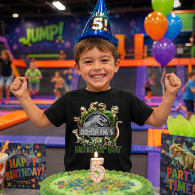 Child celebrating a birthday with a dinosaur-themed shirt and cake in an indoor playground.