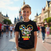 Child wearing a Disney-themed t-shirt with cartoon characters in front of a blurred theme park background.