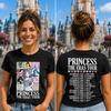 A woman stands outdoors in front of a castle, showing a black graphic T-shirt from both the front and back. The front has a colorful illustrated collage with the text 'PRINCESS THE ERAS TOUR.