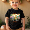 Child wearing a black t-shirt with a birthday-themed design, standing against a blurred background.