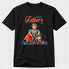 A black short-sleeve crewneck t-shirt featuring a colorful graphic of two cartoon superheroes on a light gray textured background.